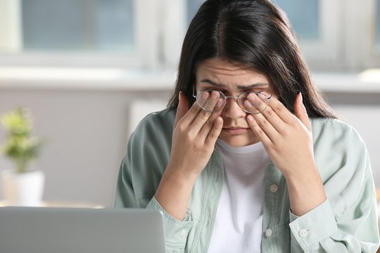 Young woman suffering from itchy eyes in office